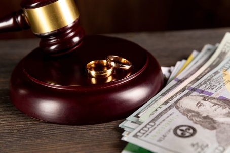 Image of gavel next to two gold rings and a small pile of money